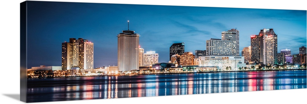 Panoramic photograph of the New Orleans skyline lit up at dusk and reflecting colorful bands onto the Mississippi River.