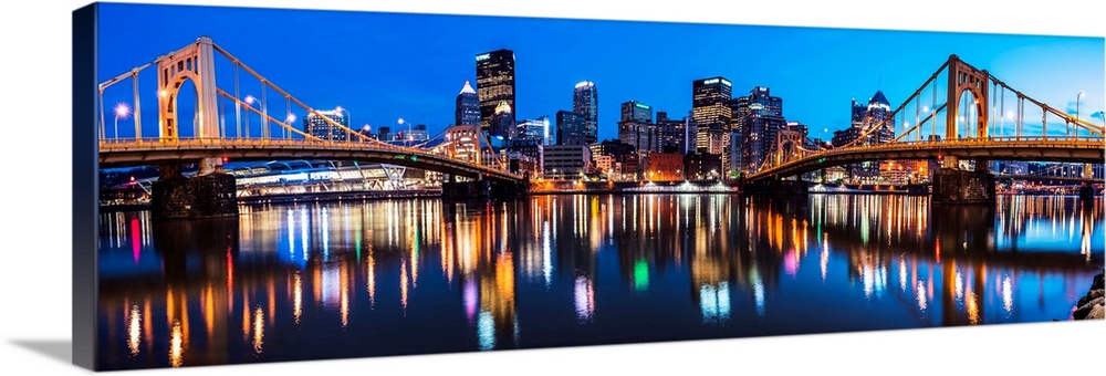Panoramic photo of downtown Pittsburgh at night with the Rachel Carson Bridge and the Andy Warhol Bridge over the Alleghen...