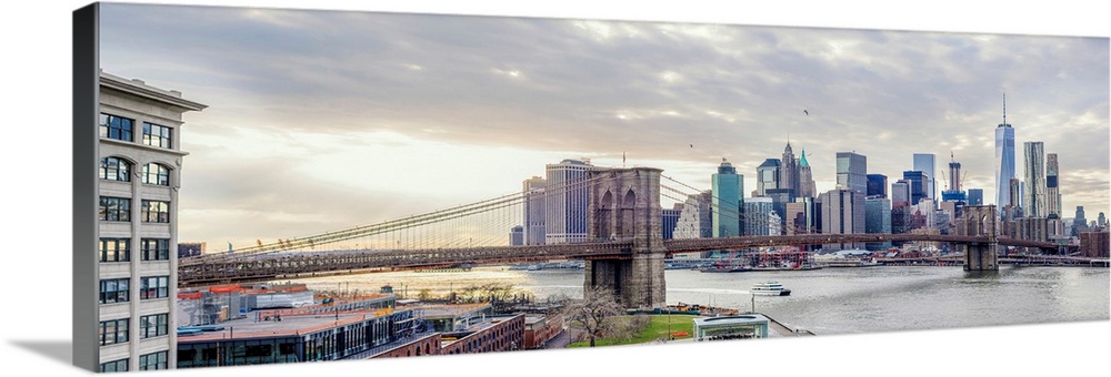 Panoramic view of the Brooklyn Bridge in New York from the east side with the sun shining through clouds.