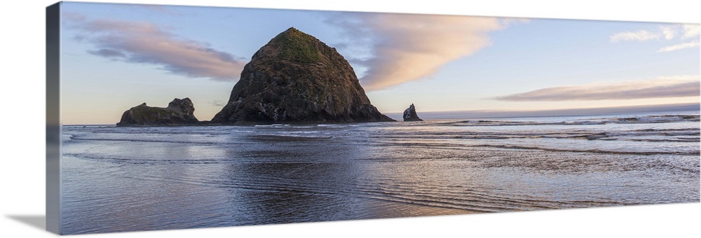 Panoramic photograph of Haystack Rock with a pink and purple sunset and reflections on the water.