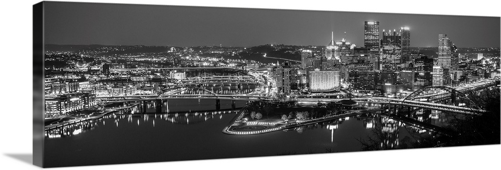 Panoramic photo of the city of Pittsburgh illuminated at night, with Point State Park in the foreground.