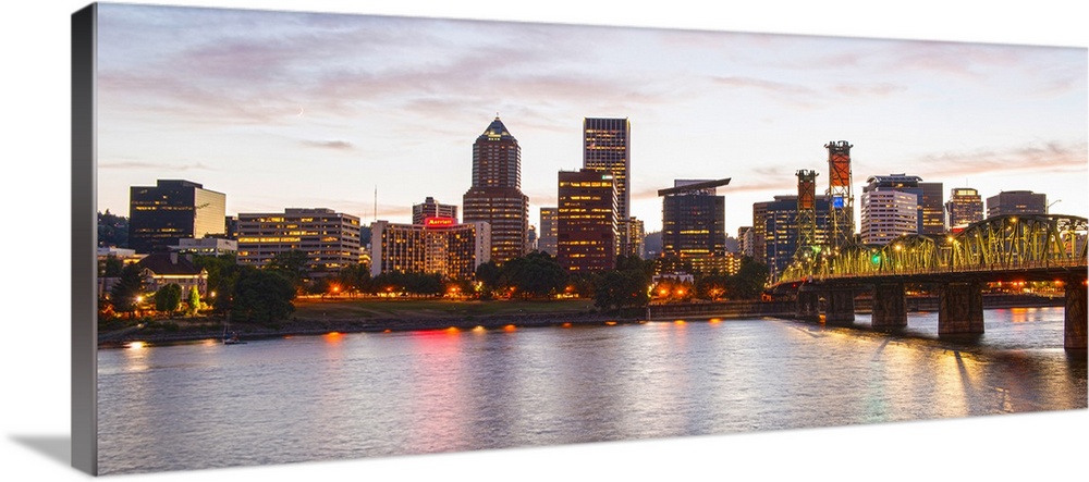 Panoramic photograph of the Portland, Oregon skyline lit up with yellow lights at the beginning of sunset with a small cre...