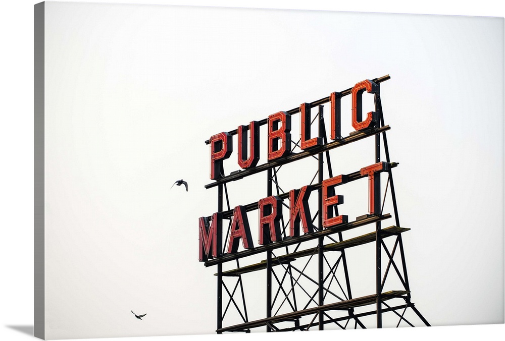 Photograph of the red Public Market sign  at the farmers market in downtown Seattle with two birds flying around it.