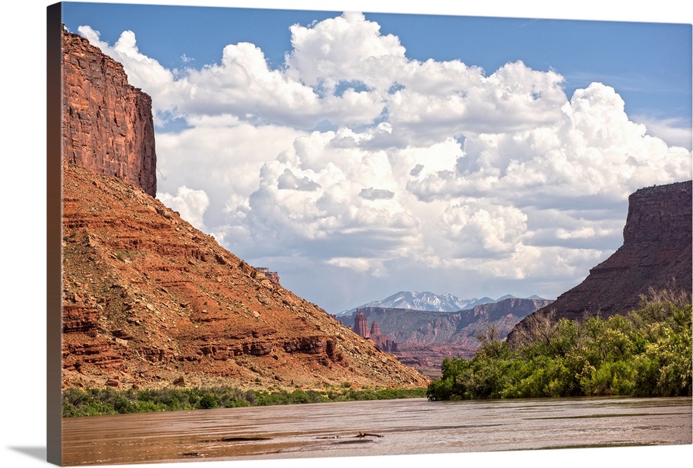 Tall sandstone cliffs tower along the edge of the Colorado River, with clouds and blue skies overhead, Canyonlands Nationa...