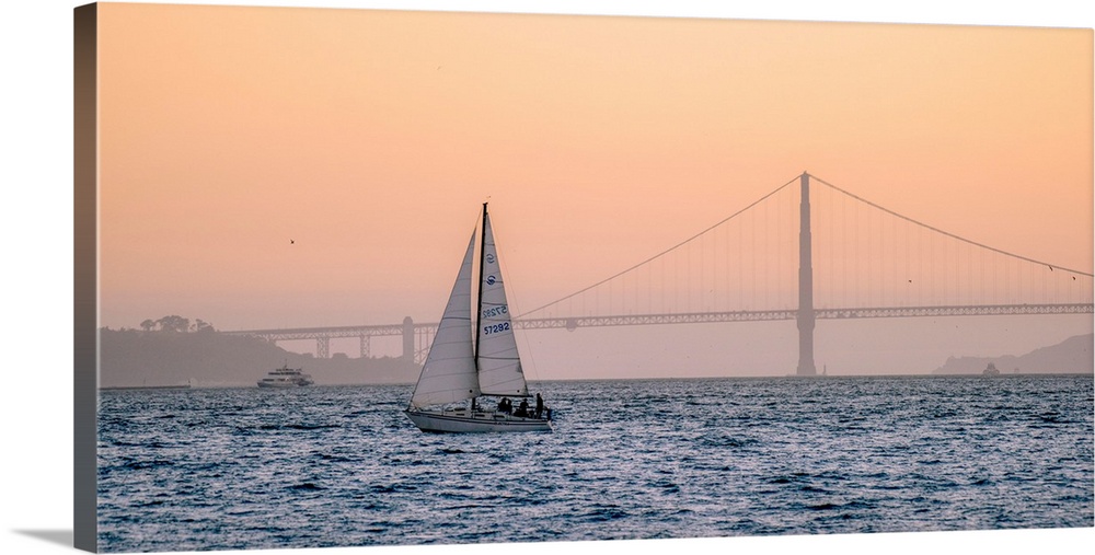 A lone sailboat floats in the pacific ocean with Golden Gate bridge in the background, San Francisco.