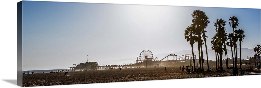 Panoramic photograph of the Santa Monica Pier in Los Angeles, California, with palm trees in the foreground and a purple h...