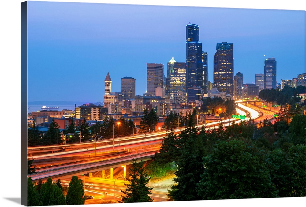 Photograph of the Seattle skyline at dusk with light trails from the cars on the highway in the foreground.