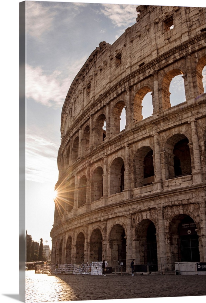 Photograph of the sun shining on the side of the Colosseum in Rome on a beautiful day.