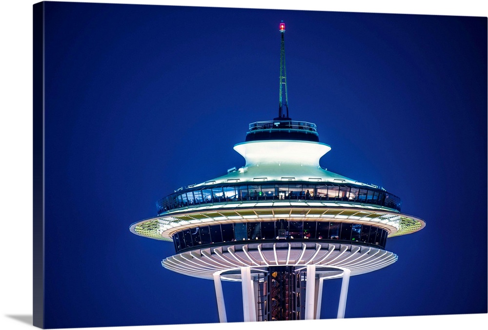 Photograph of the top of the Seattle Space Needle lit up at night on a dark purple sky.