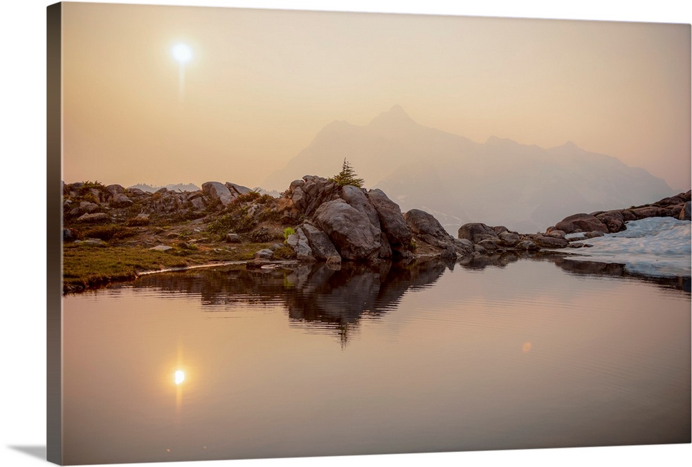 The sun rises over Mount Shuksan on a foggy day with a pond on Artist Point Trail, Washington.