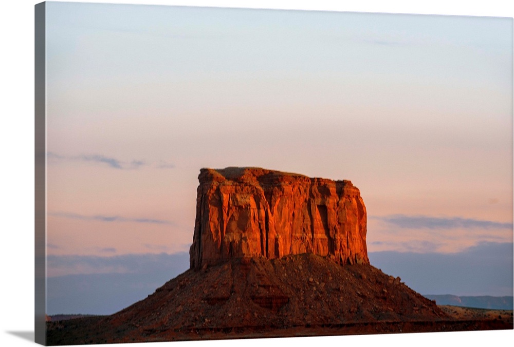 The sun sets on Mitchell Butte, highlighting the rich red sandstone In Monument Valley, Arizona.