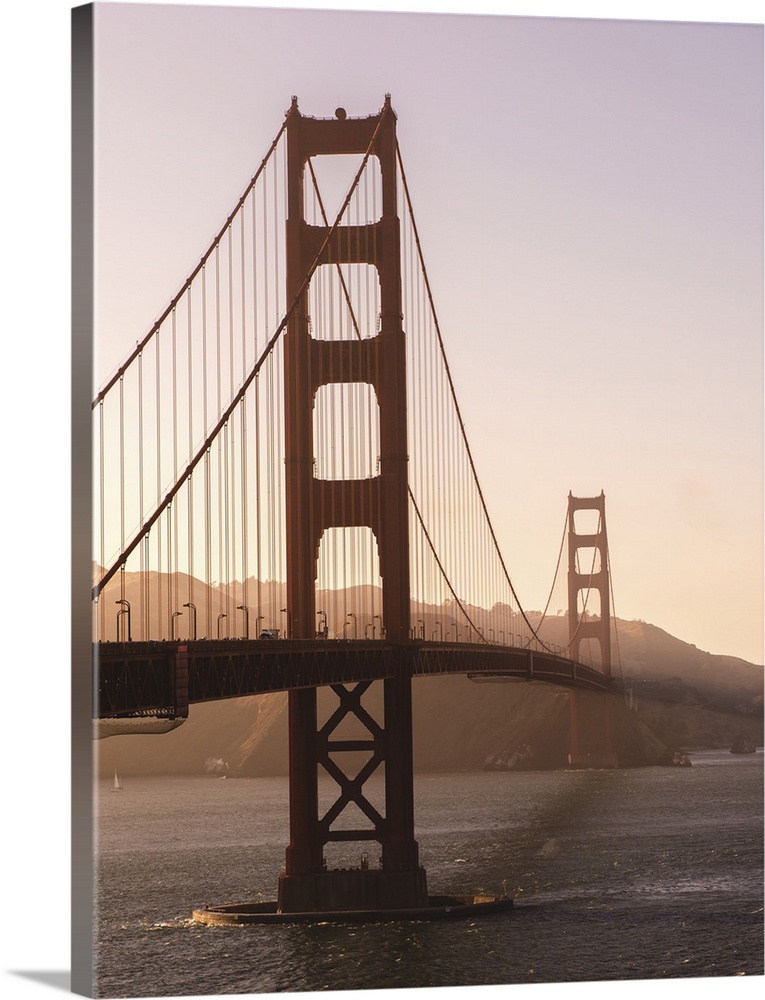 Photograph of the Golden Gate Bridge with warm hues from the sunset and light fog.