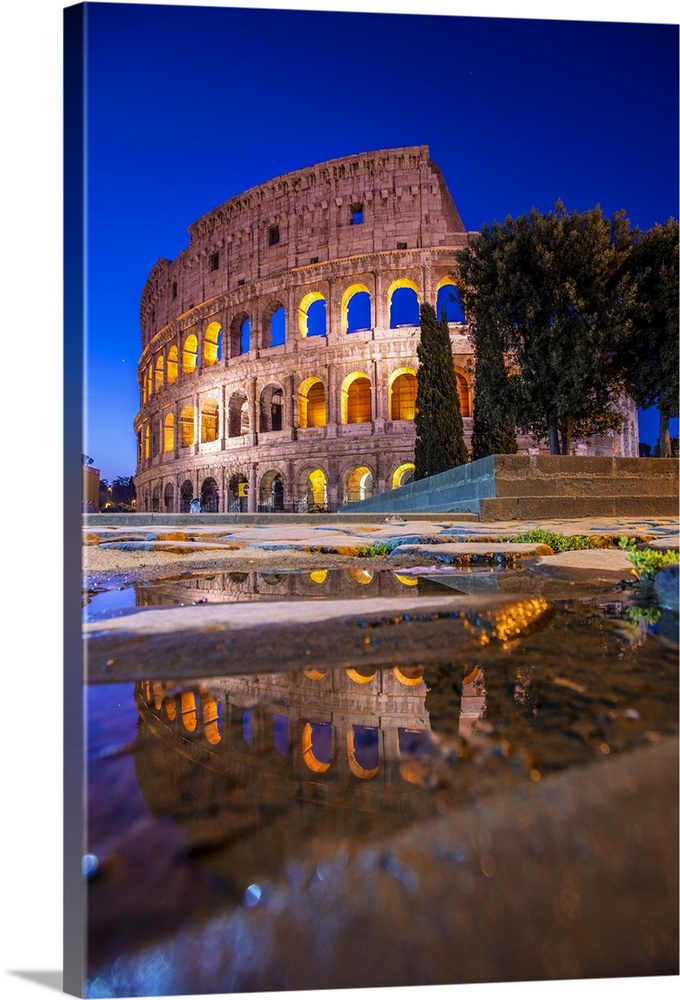 Photograph of the Colosseum at night reflecting into a puddle on the ground.