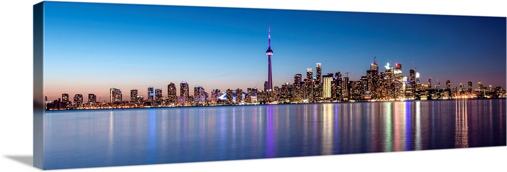 Panoramic photo of the Toronto city skyline with lights reflected in the water at night.