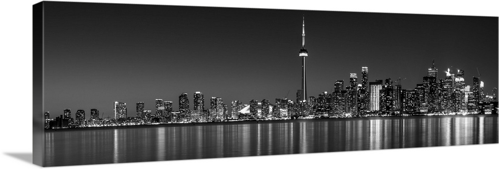 Panoramic photo of the Toronto city skyline with lights reflected in the water at night.