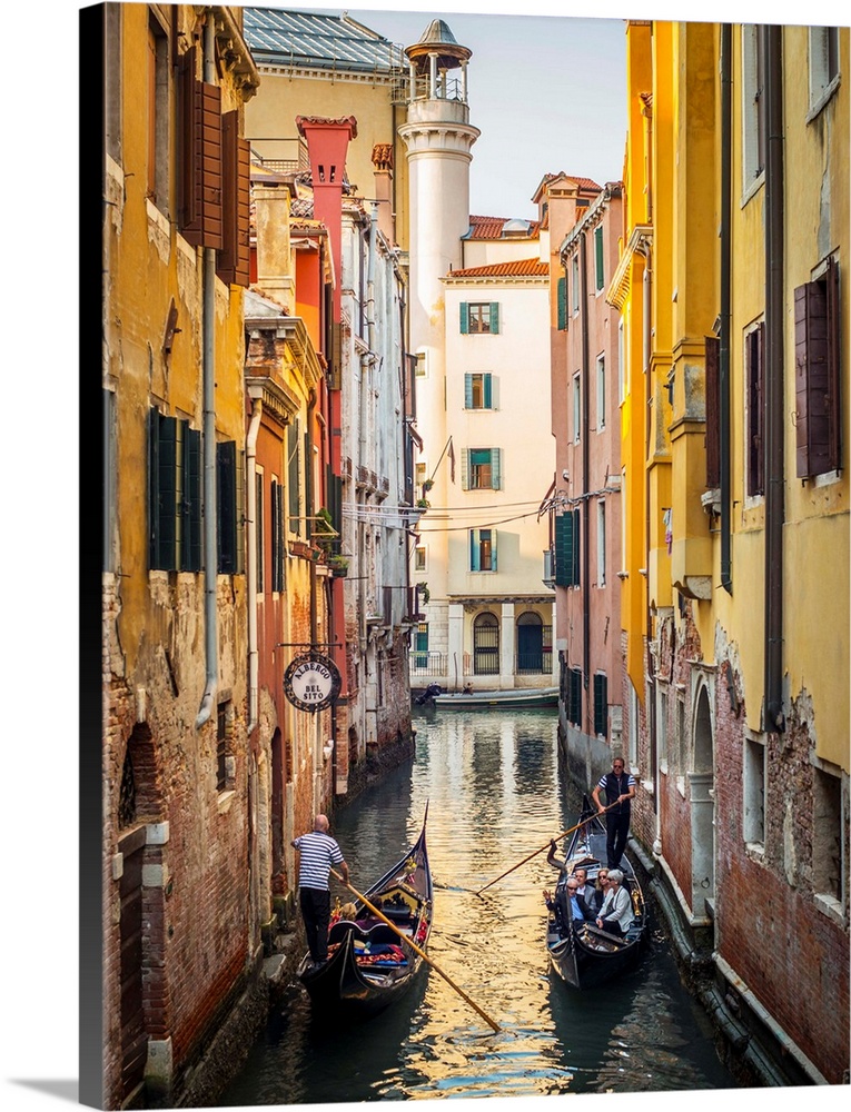 Photograph of two gondolas passing each other through a canal lined with yellow and red buildings in Venice, Italy.