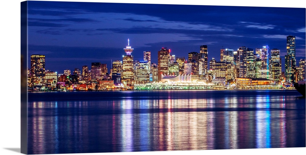 Photograph of the Vancouver, British Columbia skyline lit up on a dark blue night and reflecting bands of colorful light o...