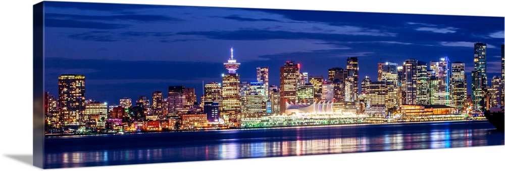 Panoramic photograph of the Vancouver, British Columbia skyline lit up on a dark purple night and reflecting bands of colo...