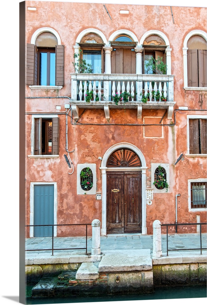 Photograph of a salmon colored facade in Venice with a door, windows, and a balcony.