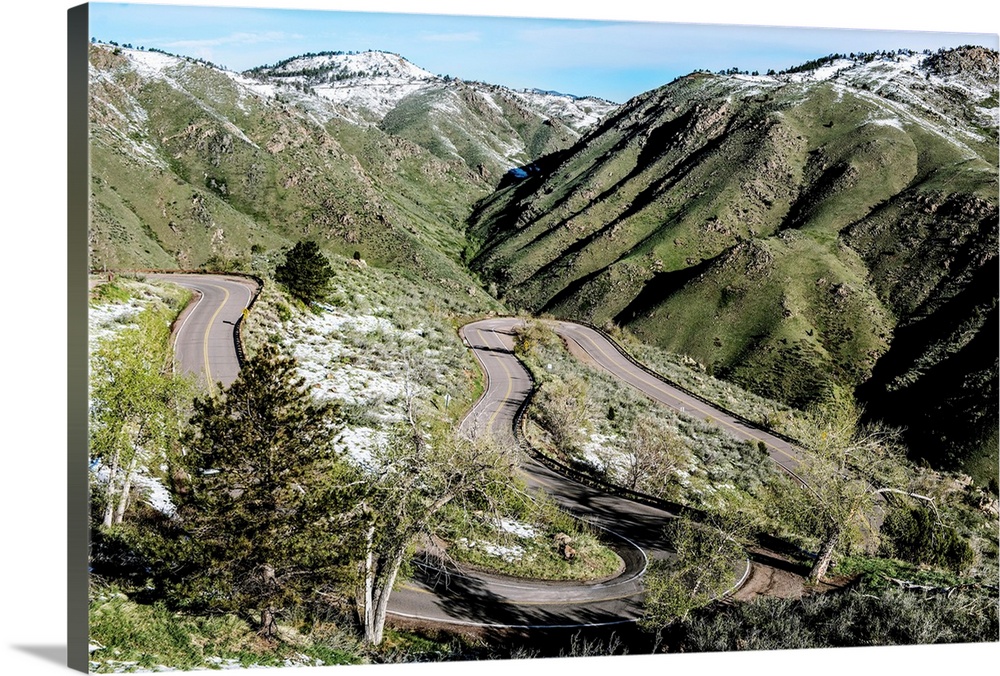 Photo of a winding road below a mountain slightly covered in snow in Colorado.