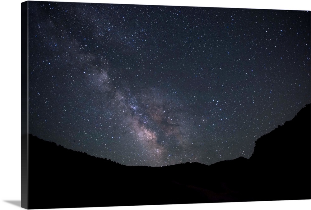 Silhouette photograph of Zion National Park at night time with a starry sky and the Milky Way above.