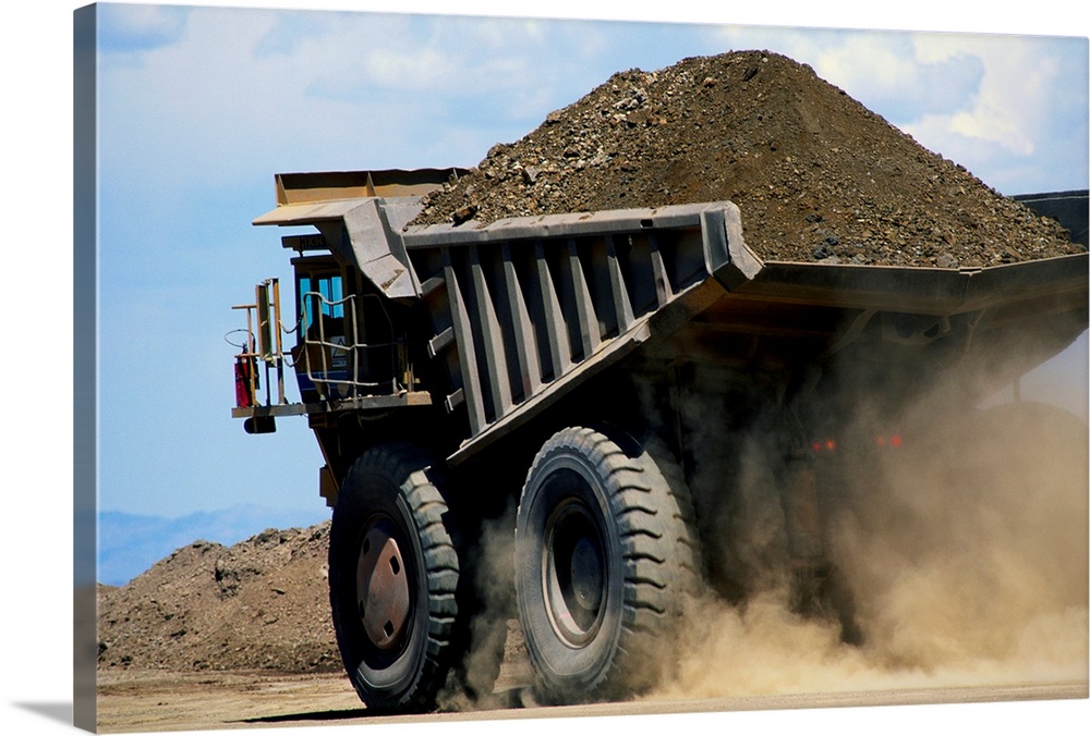 A dump truck carrying gravel kicks up a cloud of dust.