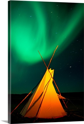 A solitary tepee is illuminated under a sky streaked with light from the aurora borealis, Northwest Territories, Canada