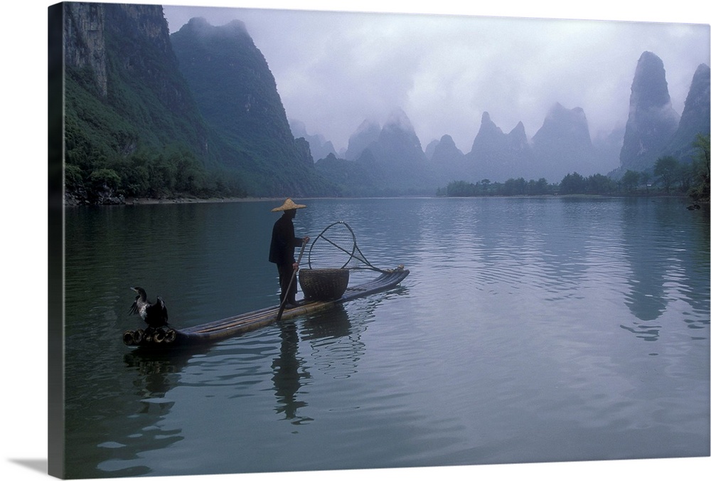 A fisherman is photographed paddling his raft toward immense cliffs that are shown through a layer of fog.