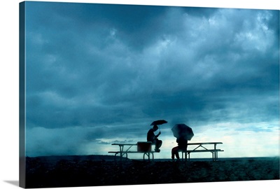 Determined park visitors sit on picnic tables while waiting out a storm