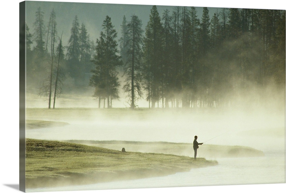 From the National Geographic Collection.  Photograph of a silhouette of a man fishing at lake's edge in the morning fog.  ...