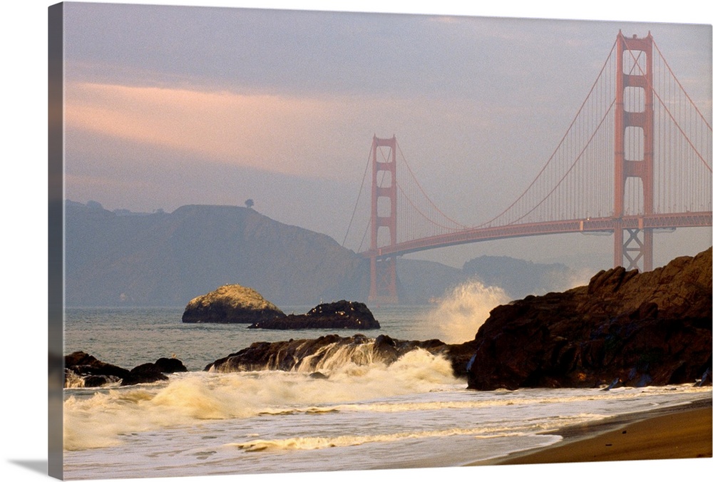 From the National Geographic Collection a landscape photograph of waves crashing on a rocky shore with famous bridge and b...