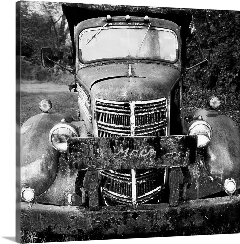 A square black and white photograph of a rusted old Mack dump truck.