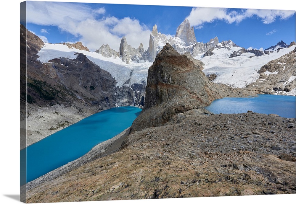 A couple in mountain gear rests on rocks with view to Lago de los Tres and Mount Fitz Roy, Patagonia, Argentina, South Ame...