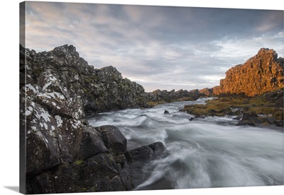A river flows from the Oxarafoss waterfall at sunrise in Thingvellir National Park