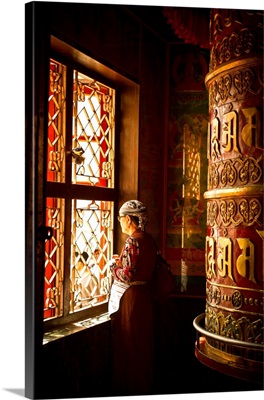 A Tibetan woman stands next to a large prayer wheel of the temple of Boudhanath Stupa