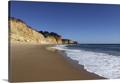 A wave washes an empty beach of golden sand, with steep cliffs, Algarve, Portugal