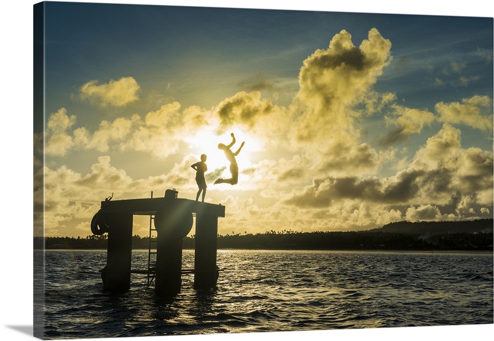 Backlit local boys jumping into the water of the lagoon of Wallis from a platform, Wallis and Futuna, Pacific