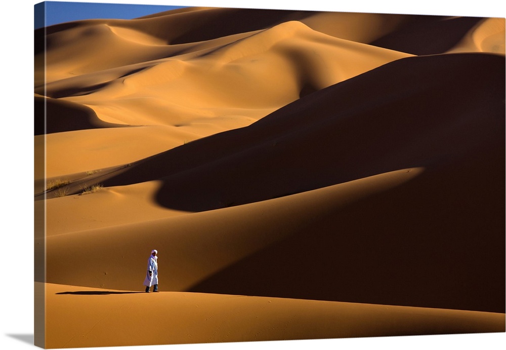Berber man walking among the orange sand dunes of the Erg Chebbi sand sea, Sahara Desert near Merzouga, Morocco, North Afr...