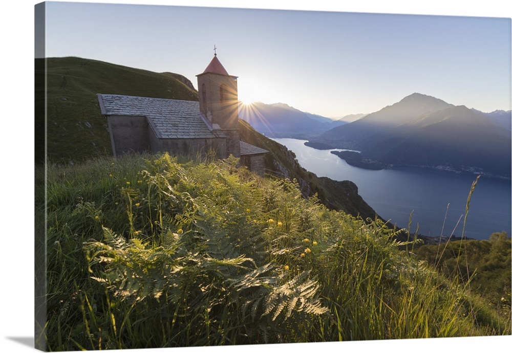 Sunbeam on Church of San Bernardo lights up the landscape around the blue water of Lake Como at dawn, Musso, Lombardy, Ita...