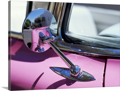 Close-up of a wing mirror and reflection on a pink Cadillac car