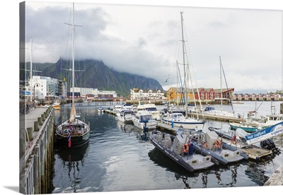 Clouds on rocky peaks with boats in the harbor of the fishing village of Svolvaer