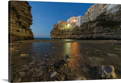 Dusk lights on the clear sea framed by the old town perched, Polignano a Mare, Italy