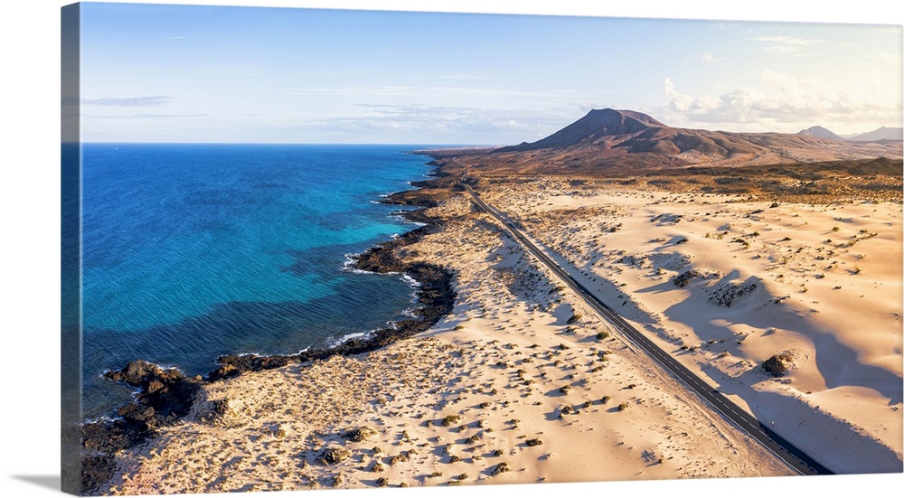 Empty road crossing the sand dunes overlooking the ocean, Corralejo Natural Park, Fuerteventura, Canary Islands, Spain, At...