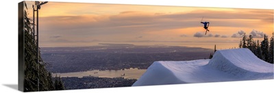 Freestyle skier doing a trick off a jump above city at sunset, Canada