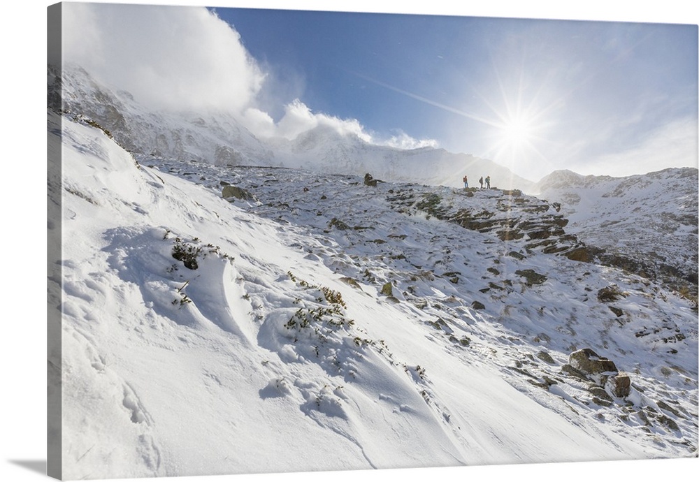 Hikers proceed in the snowy valley of Alpe Fora, Malenco Valley, Province of Sondrio, Valtellina, Lombardy, Italy
