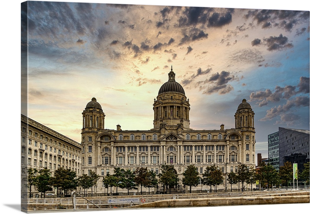 Historic building with domes against a dramatic sunset sky, flanked by trees and a water feature in Liverpool, Merseyside,...