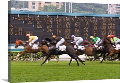 Horses race past large scoreboard during race at Happy Valley racecourse, Hong Kong