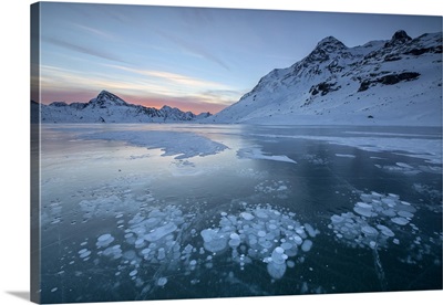 Ice bubbles frame the snowy peaks reflected in Lago Bianco, Engadine, Switzerland