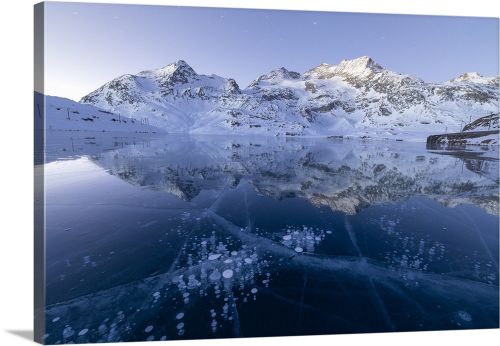 Ice bubbles frame the snowy peaks reflected in Lago Bianco, Bernina Pass, canton of Graubunden, Engadine, Switzerland