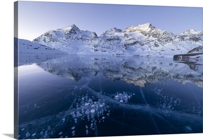 Ice bubbles frame the snowy peaks reflected in Lago Bianco, Engadine, Switzerland